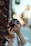 A person is holding a camera up to their face, seemingly focused on capturing a photograph. The surroundings are slightly blurred, with natural elements suggesting an outdoor setting. The person's concentration is evident as they adjust the camera settings.