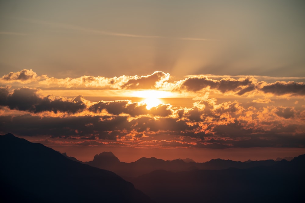 mountains under orange sky with sun rays piercing through clouds