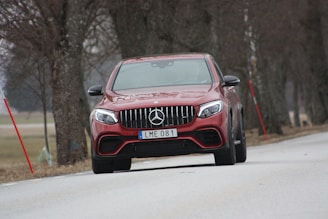red Mercedes-Benz vehicle on roadway near trees