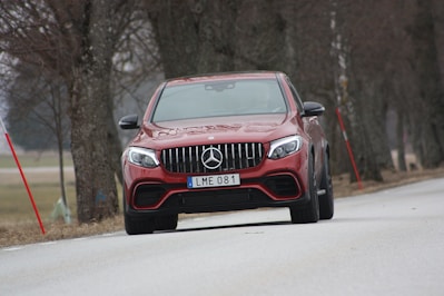red Mercedes-Benz vehicle on roadway near trees