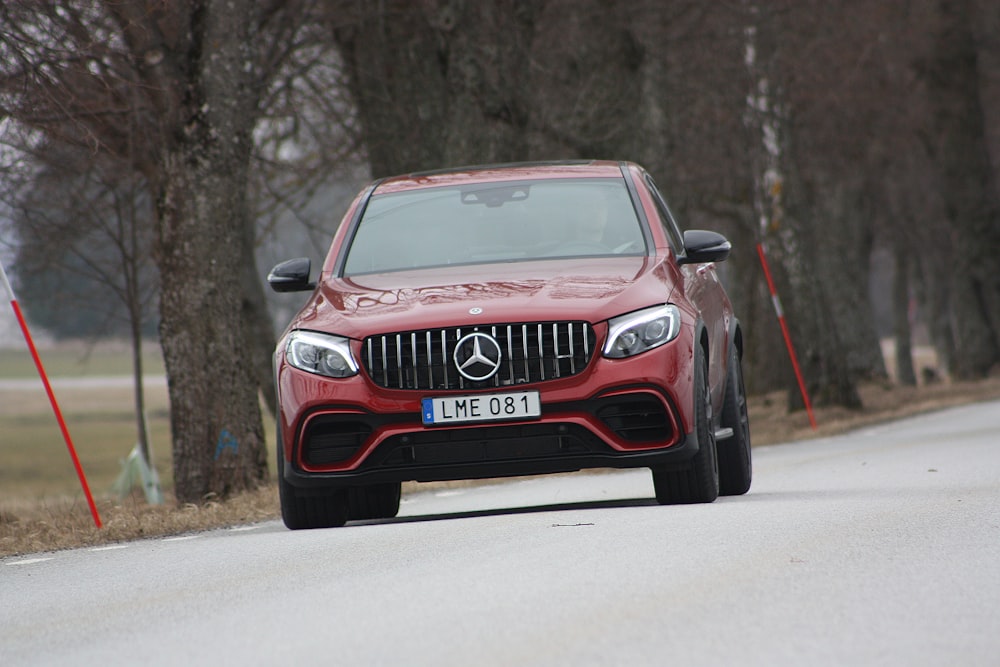 red Mercedes-Benz vehicle on roadway near trees