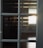 Sunlight streams through blinds, reflecting on a set of multi-paneled glass windows. The light casts distinct horizontal shadows that create a warm pattern against dark glass and wooden flooring.