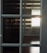 Sunlight streams through blinds, reflecting on a set of multi-paneled glass windows. The light casts distinct horizontal shadows that create a warm pattern against dark glass and wooden flooring.