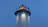 Close-up of a lighthouse beacon shining golden light over dark navy waves at dusk.