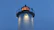 Close-up of a lighthouse beacon shining golden light over dark navy waves at dusk.