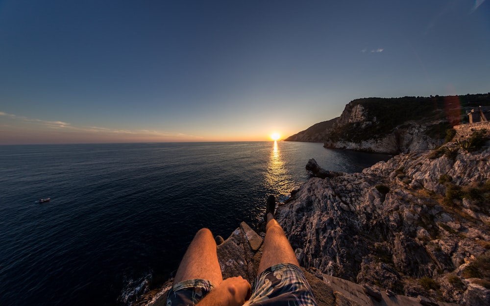person sitting on cliff in front of sea