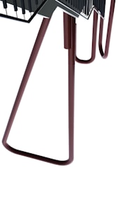 A large metallic structure with elongated legs, somewhat appearing like a chair or table. The design is abstract and industrial with a minimalistic look. The structure is composed of tubular brown legs leading up to a flat, darker surface with railing details.
