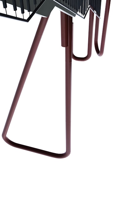 A large metallic structure with elongated legs, somewhat appearing like a chair or table. The design is abstract and industrial with a minimalistic look. The structure is composed of tubular brown legs leading up to a flat, darker surface with railing details.