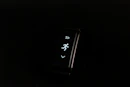 A digital fitness tracker with a black band is displayed against a dark background. The screen features minimalistic white icons for navigation and an exercise mode, including an arrow, a running figure, and a downward-pointing arrow.