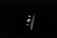 A digital fitness tracker with a black band is displayed against a dark background. The screen features minimalistic white icons for navigation and an exercise mode, including an arrow, a running figure, and a downward-pointing arrow.