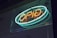 A neon sign with the word 'open' written in bright orange and blue lights is mounted on a glass surface. The sign is illuminated, casting a subtle glow in the surrounding area, creating a vibrant and inviting atmosphere.