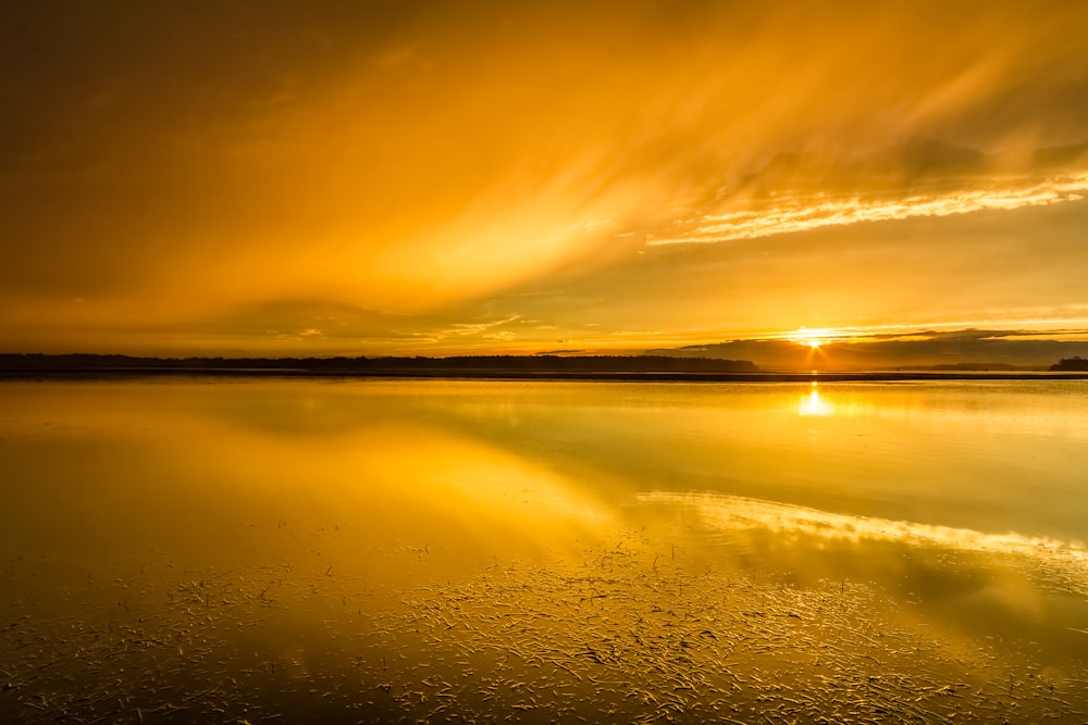 body of water under white clouds during golden hour