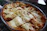A freshly baked dish of lasagna is presented in a glass baking dish. The top is golden brown with melted cheese and crispy edges, indicating it has just come out of the oven. The layers of pasta and filling are visibly rich and inviting.