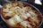 A freshly baked dish of lasagna is presented in a glass baking dish. The top is golden brown with melted cheese and crispy edges, indicating it has just come out of the oven. The layers of pasta and filling are visibly rich and inviting.