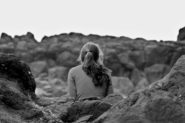 grayscale photography of woman sitting on rock