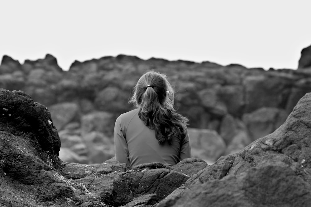 grayscale photography of woman sitting on rock