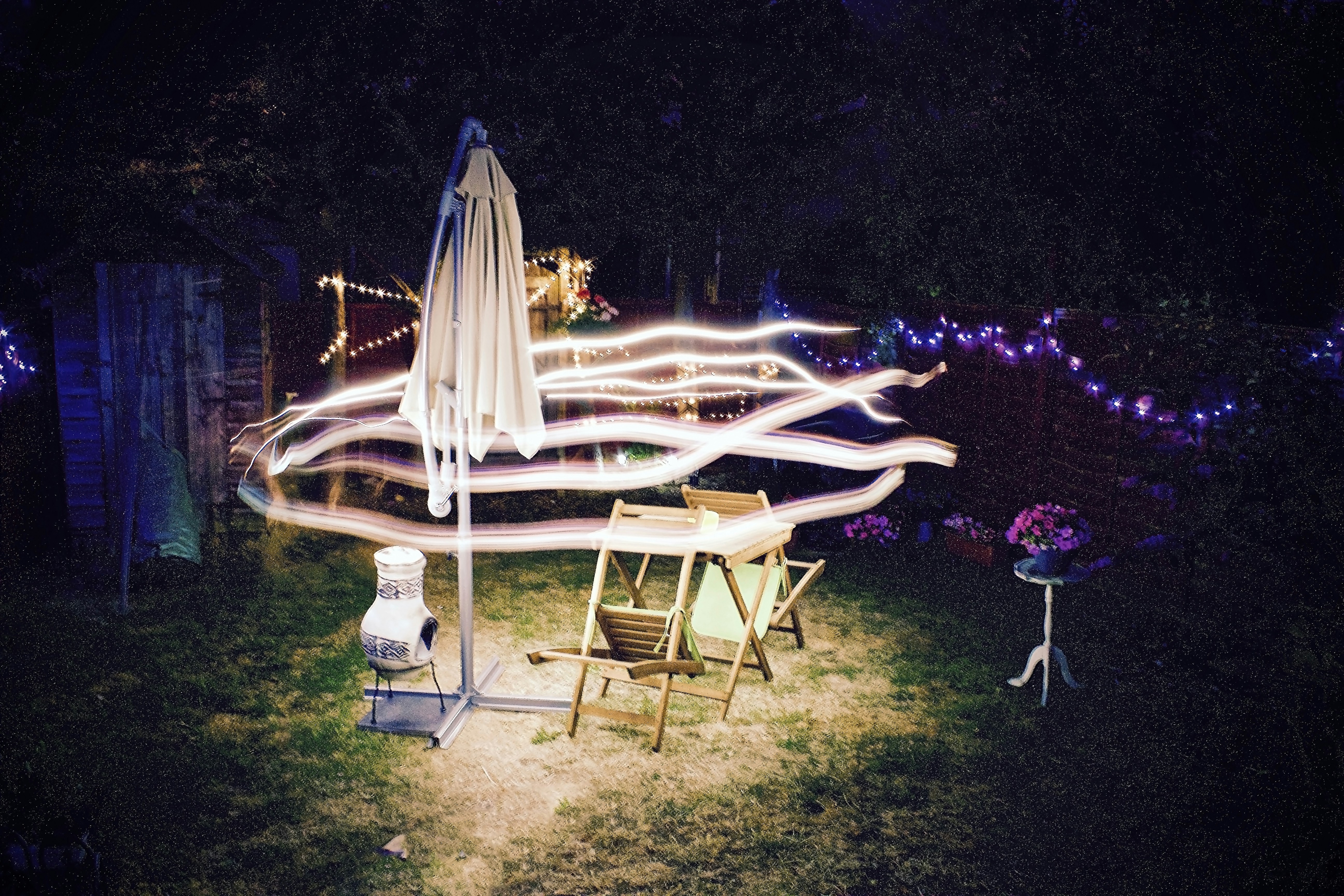 time lapse photography of lights over cantilever parasol and folding chairs at nighttime