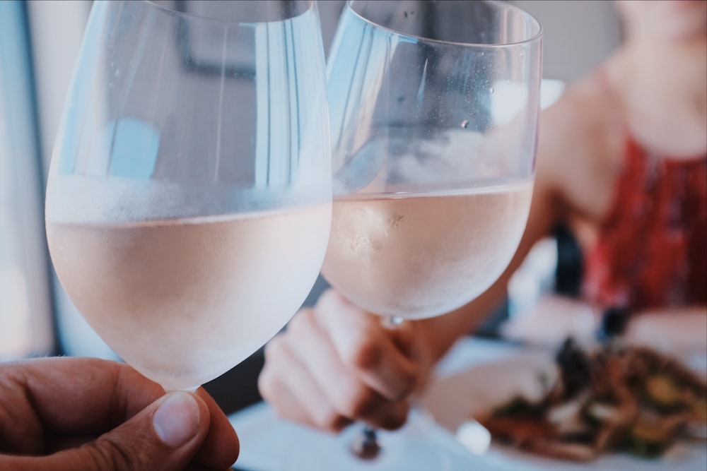duas pessoas brindando taças de vidro de vinho