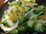 A close-up view of a fresh vegetable mix containing broccoli florets, sliced yellow bell peppers, and thinly sliced onions.