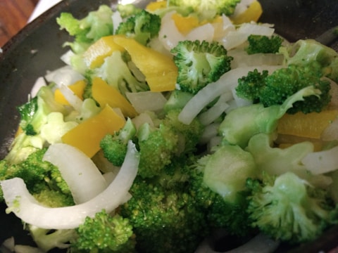 A close-up view of a fresh vegetable mix containing broccoli florets, sliced yellow bell peppers, and thinly sliced onions.