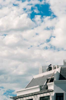 Technician inspecting a modern HVAC unit on a residential rooftop under clear skies.