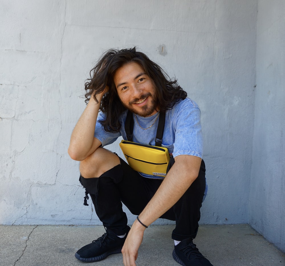 man sitting beside wall while holding his long hair