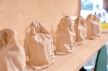 Several small beige drawstring bags lined up in a row on a textured surface. The bags appear to be made of a natural fabric and have simple black geometric designs printed on them.