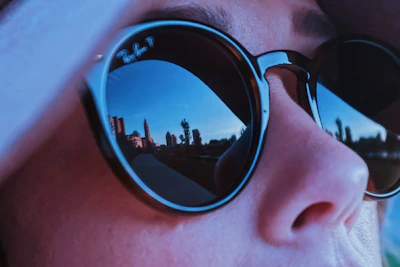 Person wearing trendy sunglasses outdoors on a sunny day with a city background.