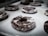 Several chocolate donuts with a dusting of powdered sugar are resting on a baking sheet lined with parchment paper. The donuts are arranged in rows and appear to be freshly baked.