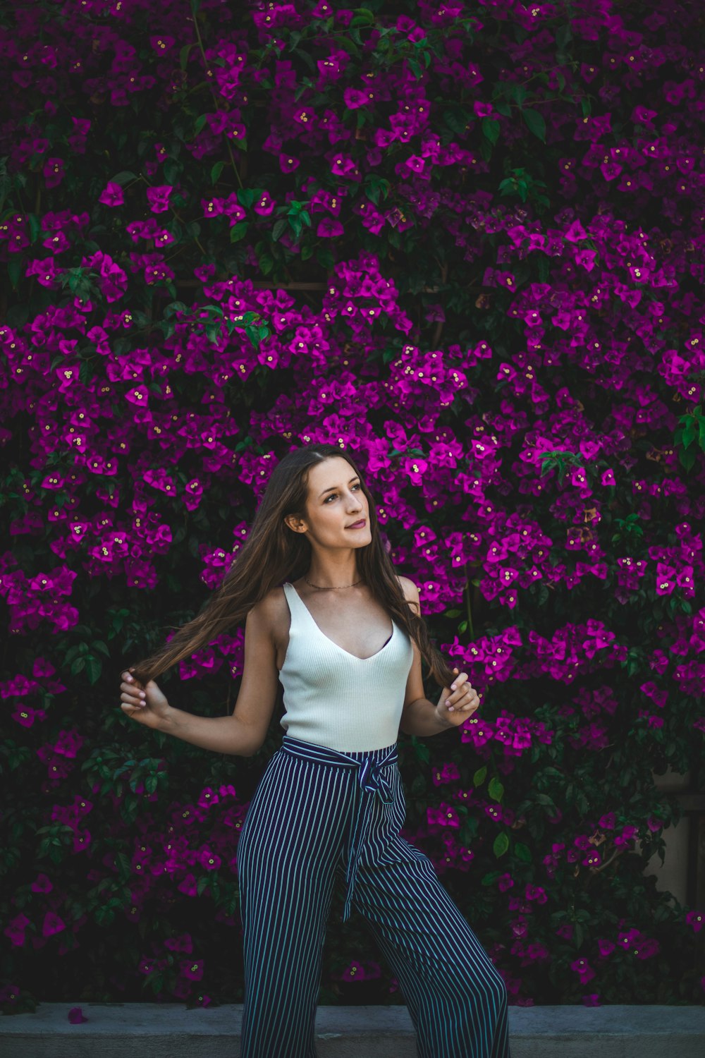 mujer sonriente sosteniendo su cabello frente a flores púrpuras durante el día