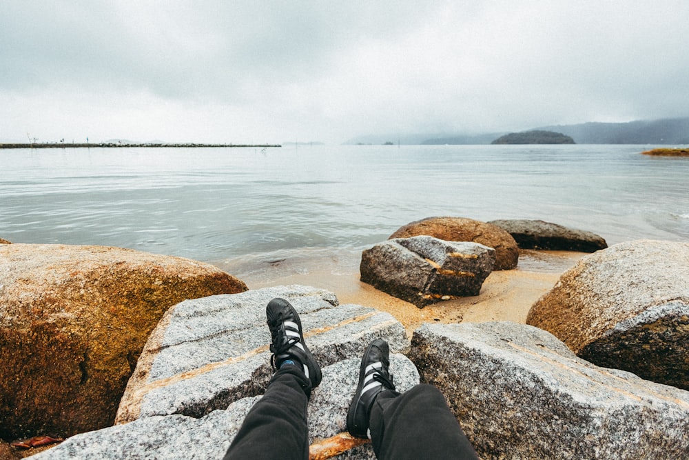 man sitting on gray stone beside the seashoee