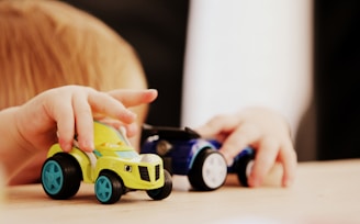 child playing with two assorted-color car plastic toys on brown wooden table