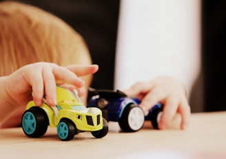 child playing with two assorted-color car plastic toys on brown wooden table