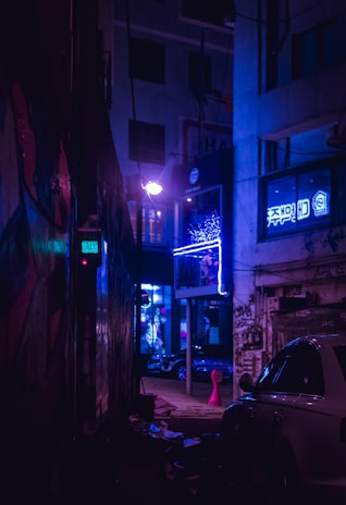 A moody urban street scene at night with graffiti walls illuminated by red neon lights.