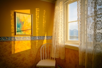 white chair placed beside window with curtain