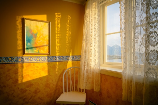 white chair placed beside window with curtain