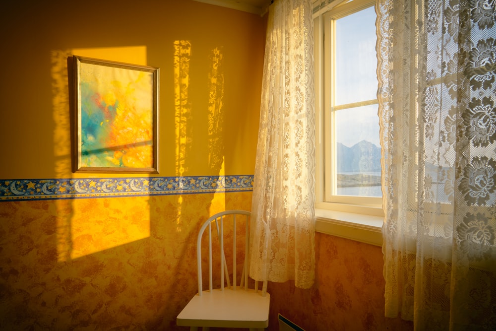 chaise blanche placée à côté de la fenêtre avec rideau