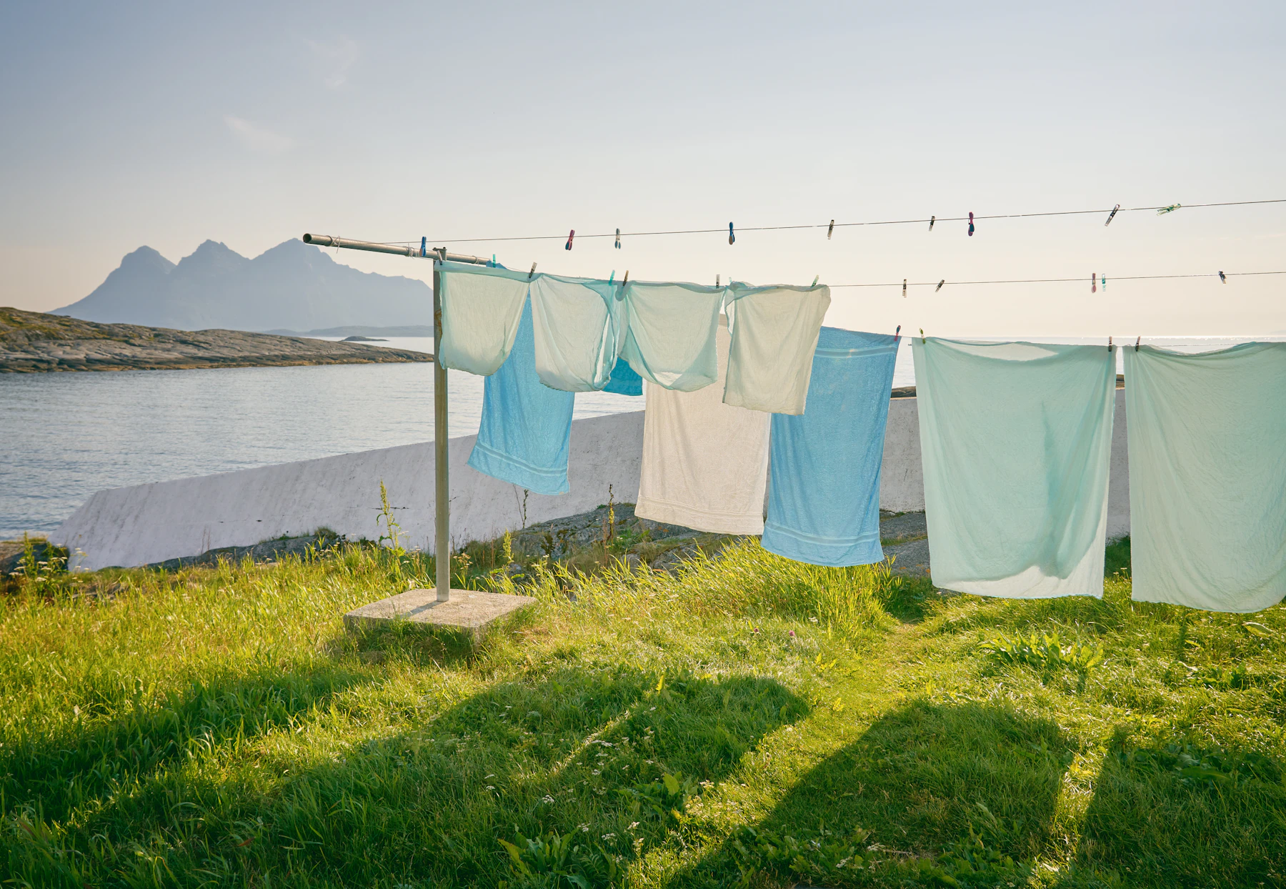 Pale blue and white washing on a line in a green field by the sea