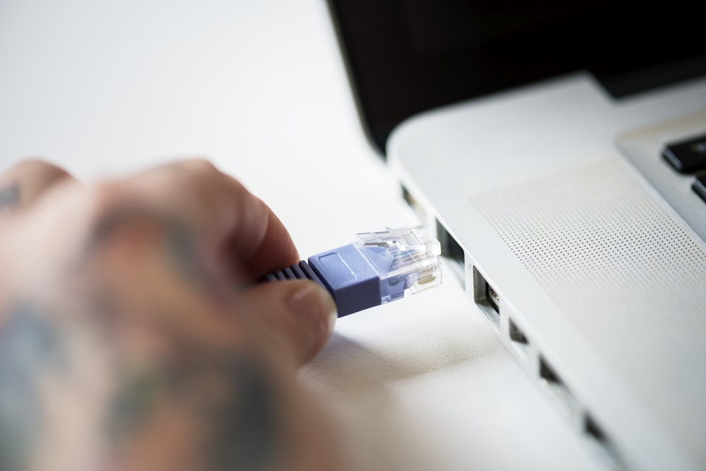 person attaching RJ45 cable on white laptop