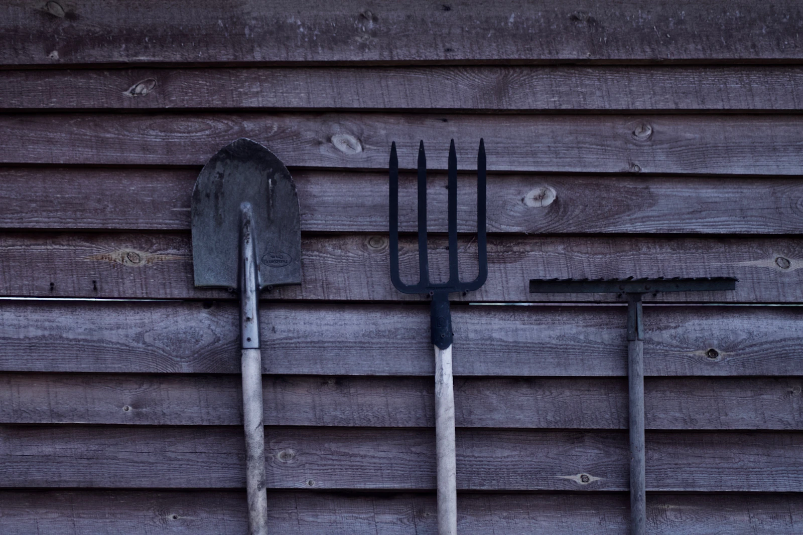 Brown shovel and two rakes on a wooden surface