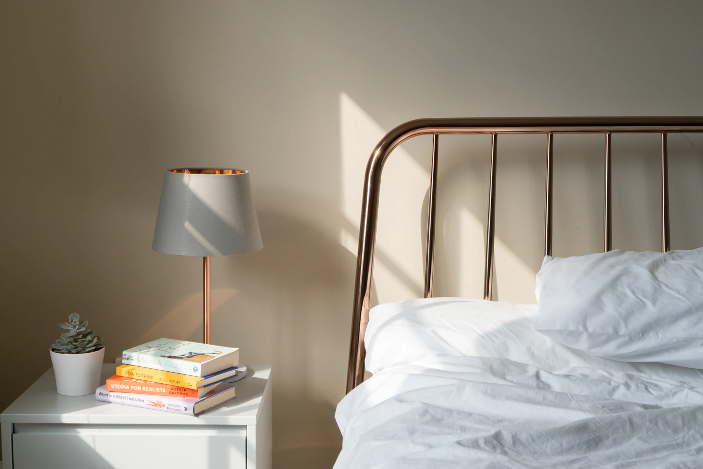 Warm morning sunlight falling across a cosy bedroom with a brass bed, bedside lamp, plant and books
