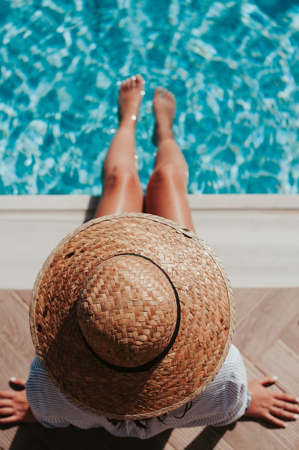 Legs in a glistening pool and a beach hat covering a face showing one of several summer activities