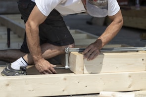 Team member carefully measuring and nailing framing wood on a new home site.