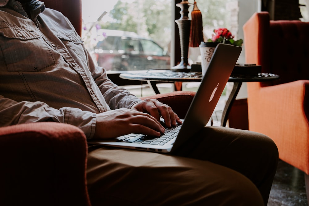 MacBookを膝の上に乗せて座っている男性