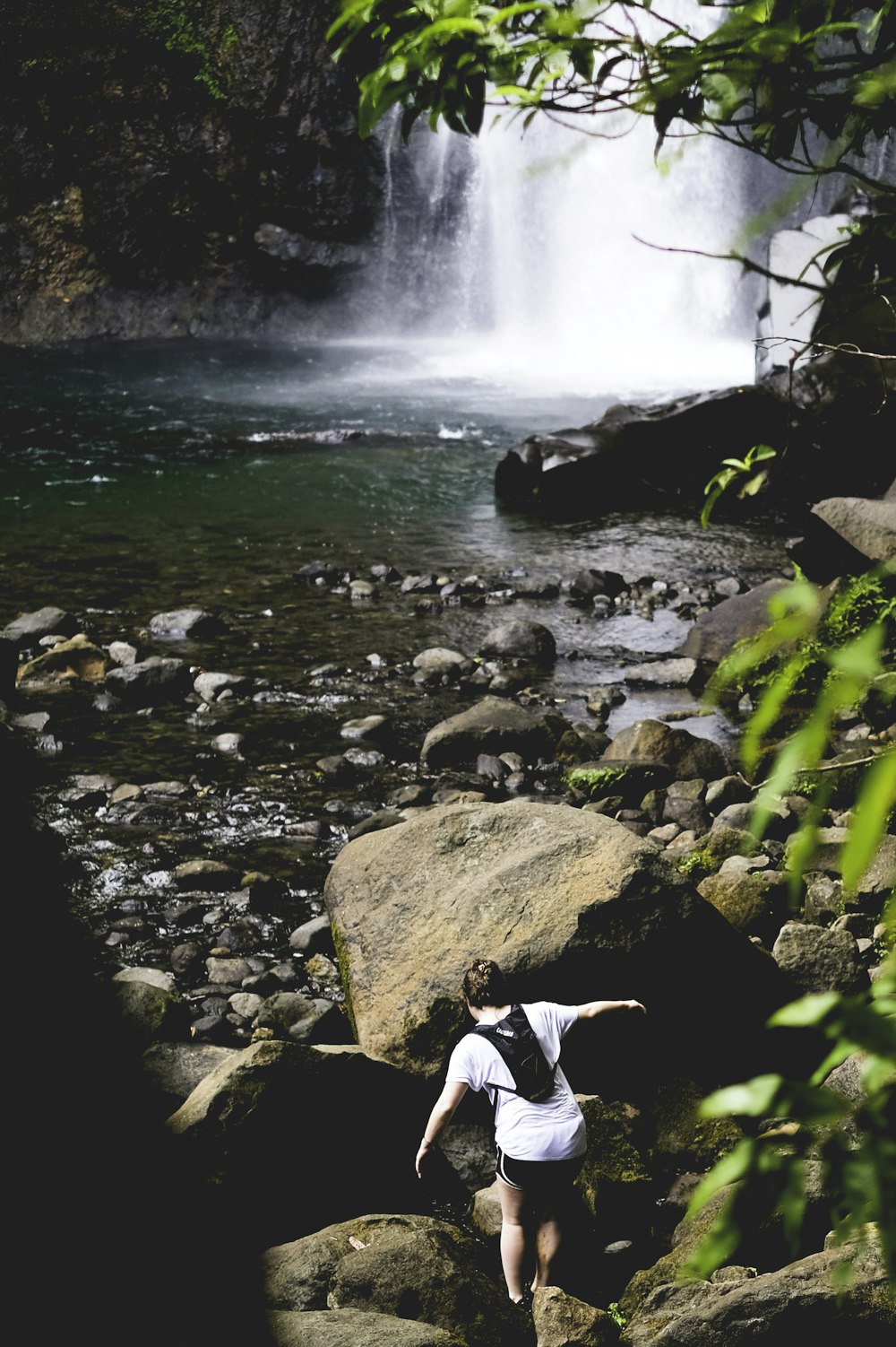 person walking on rocks near waterfall