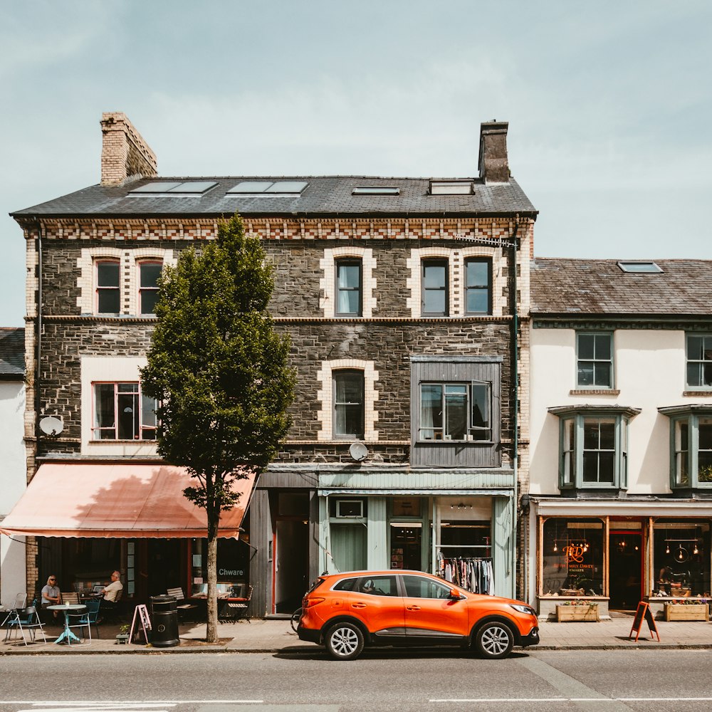 SUV orange à côté d’une maison marron et grise