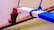 A close-up of a boat's outrigger with a wooden beam painted in red, white, and blue colors. The beam is secured with bright blue ropes, and the background shows calm, greenish water.
