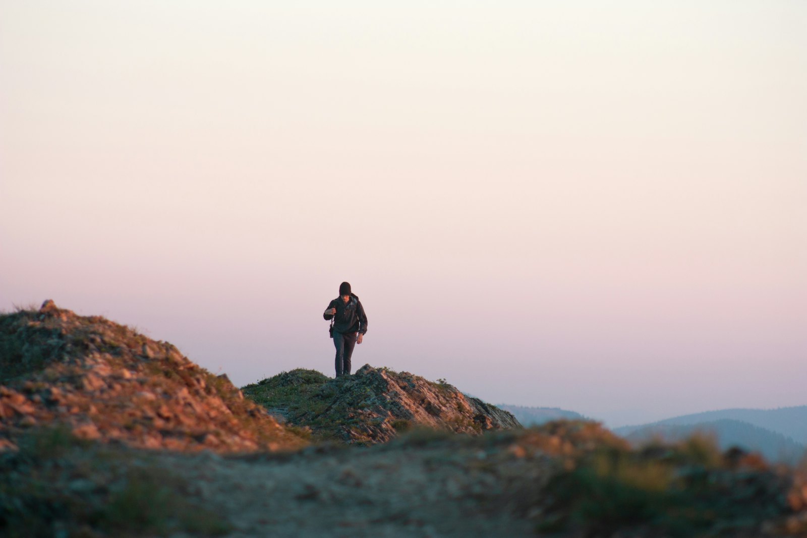 Lone figure seen from behind on a rocky outcrop at last light