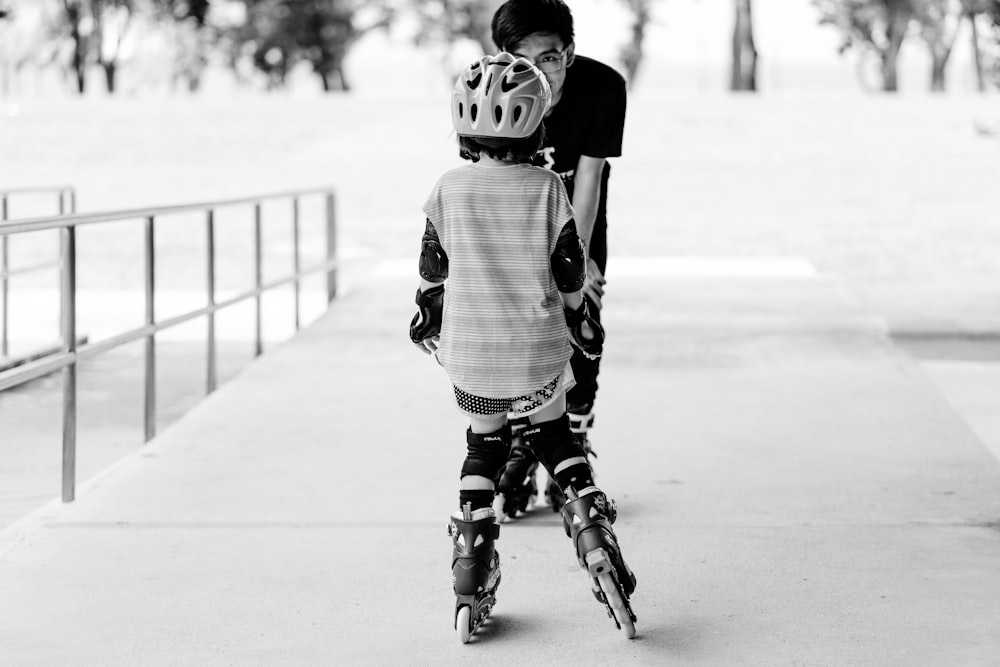 grayscale photo of man and girl using inline skates near railings