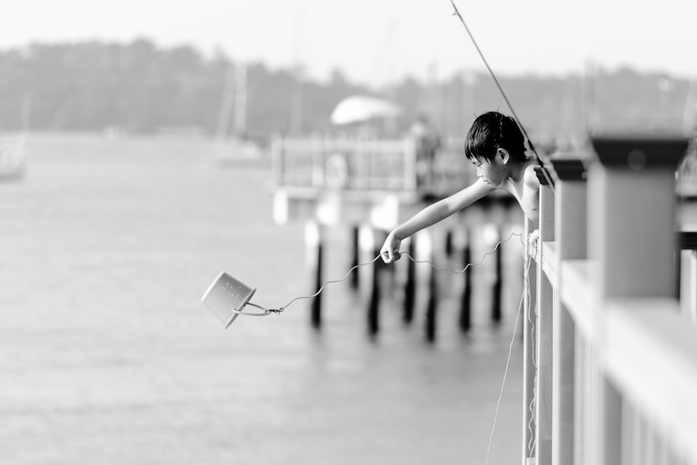 grayscale photography of boy throwing pail at the body of water